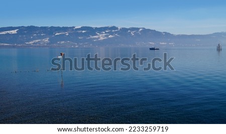 empty harbour of Lindau island on tranquil lake Constance or lake Bodensee with the Austrian Alps in the background on a fine winter evening with blue sky reflected in the water (Germany)              Royalty-Free Stock Photo #2233259719