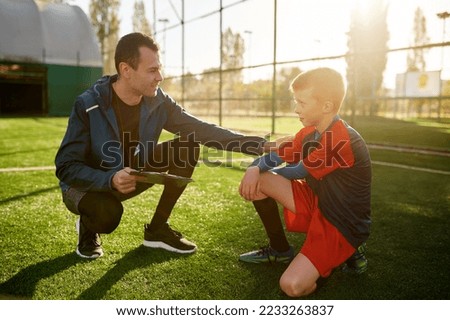Young soccer coach giving support to little football player Royalty-Free Stock Photo #2233263837