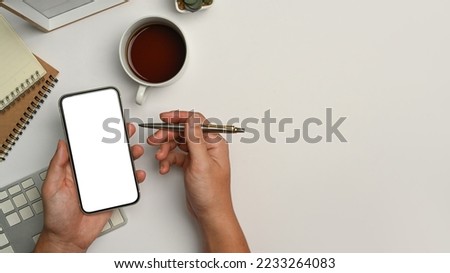 Above view of man hand holding pen and using mobile phone on white office desk
