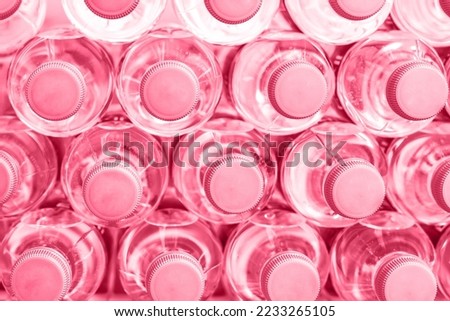 Rows of many transparent plastic bottles with drinking water supply in white refrigerator toned Color of the year 2023 Viva Magenta. Healthcare and dehydration prevention. Mineral water stack storage