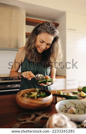 Vegetarian woman smiling while adding avocado to her buddha bowl. Senior woman serving herself a delicious vegan meal at home. Woman taking care of her aging body with a healthy plant-based diet. Royalty-Free Stock Photo #2233265285