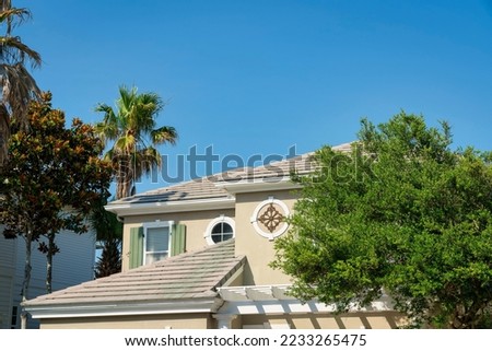 Top exterior of a house with asphalt composite roof shingles at Destin, Florida. There are trees outside the house with round trims with decorative panels and windows and a window with fake shutters.