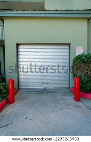 Destin, Florida- Steel roll-up door of a utility garage in a hotel. Utility garage exterior of a hotel with painted olive green wall and a concrete entrance with two red post and plants on the right.