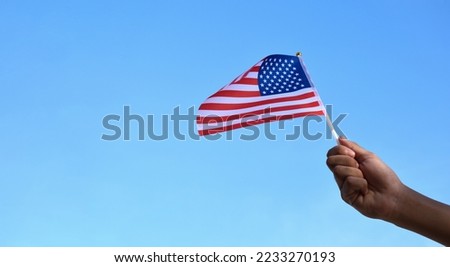 American national flag holding in hand and waving on blue sky background, soft and selective focus.