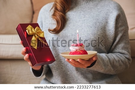 Closeup image of a young woman holding a gift box and birthday cake with candle