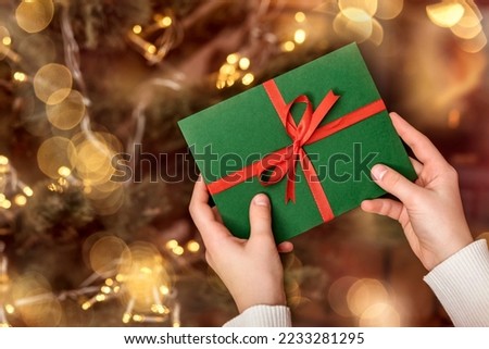 Christmas Gift Certificate or New Year Gift Envelope in Girls hands on Christmas Lights Background. Christmas Present Letter to Santa on Cristmas Tree. Copy Space