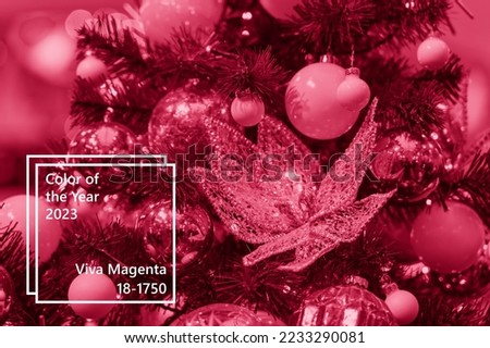 Close up of glitter flower decoration and christmas balls hanging on illuminated fir tree. Image toned in trendy pantone color of year 2023 Viva Magenta.