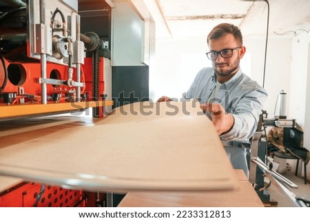 Working with wooden sheets. Man in print house that in white clothes is indoors.
