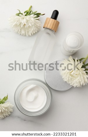Glass jar of face cream and other cosmetic products on white marble table, flat lay
