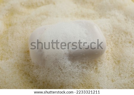 Soap with fluffy foam on yellow background, closeup