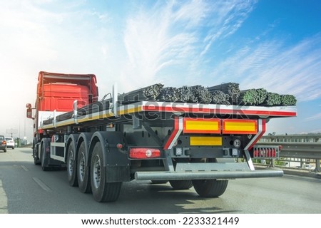 Truck with a long trailer loaded with metal rebar frame for the construction of a building drives along the highway Royalty-Free Stock Photo #2233321449