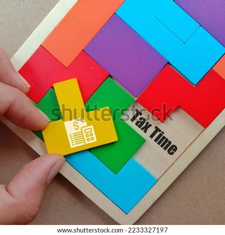 Hand holding yellow puzzle and text TAX TIME at space of wooden puzzle isolated brown background 