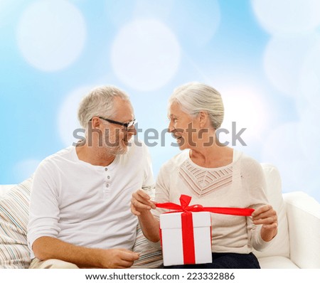 family, holidays, christmas, age and people concept - happy senior couple with gift box over blue lights background