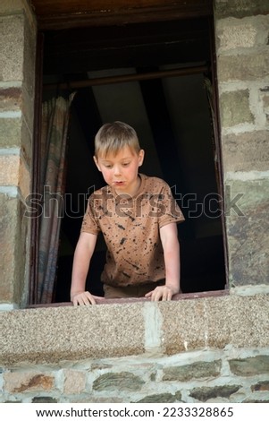 emotional eight-year-old boy looks out of the window of an old building in summer