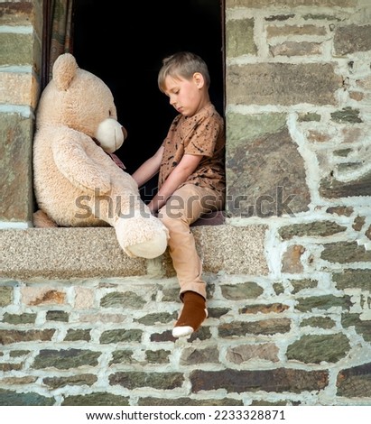 an eight-year-old boy sits in an open window with a teddy bear