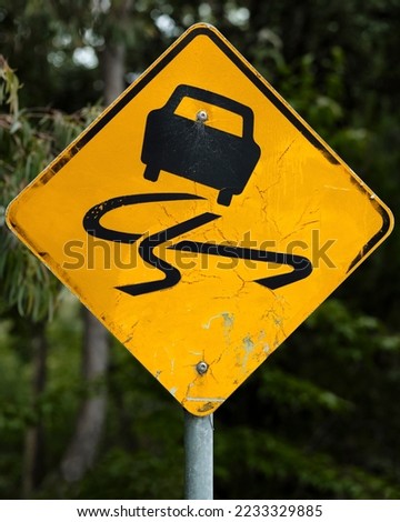 "Slippery when wet" road sign. Yellow warning sign with cracked and peeling yellow reflective surface. Black car icon cautioning of slippery road conditions