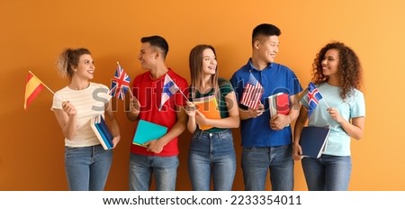 Young students of language school on orange background Royalty-Free Stock Photo #2233354011