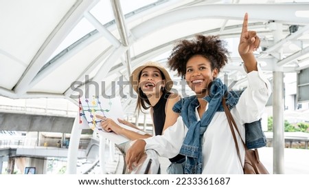 Stylish city portrait of two friend fashionable girls walking in station modern city centre. Diversity friends traveling with backpack, map, camera, making photo, tourist, get a lost, place for text. Royalty-Free Stock Photo #2233361687