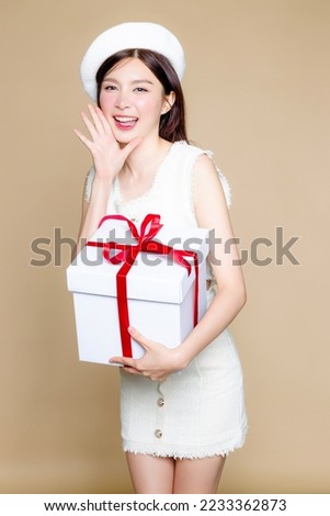Cute Asian woman smile and holding white gift box. Pretty girl model wearing white beret and natural makeup on beige background. Cosmetology, beauty and spa, wellness, Plastic surgery.