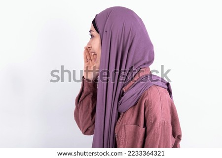 young beautiful woman wearing hijab and pink overshirt over white background look empty space holding hand near her face and screaming or calling someone.