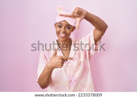 African american woman wearing sleep mask and pajama smiling making frame with hands and fingers with happy face. creativity and photography concept. 