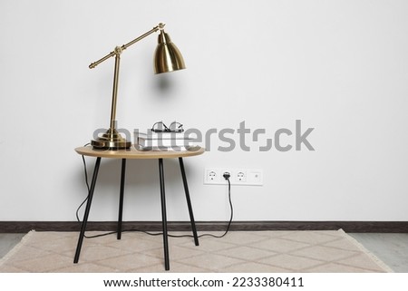 Lamp with books on wooden table near white wall, space for text Royalty-Free Stock Photo #2233380411