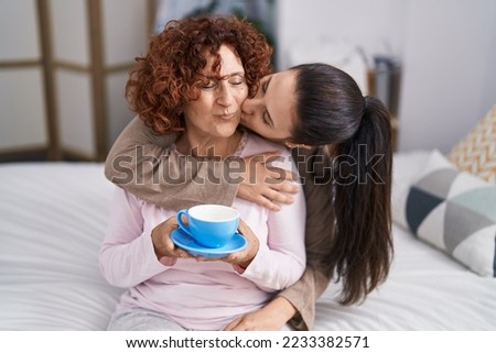 Two women mother and daughter drinking coffee sitting on bed 