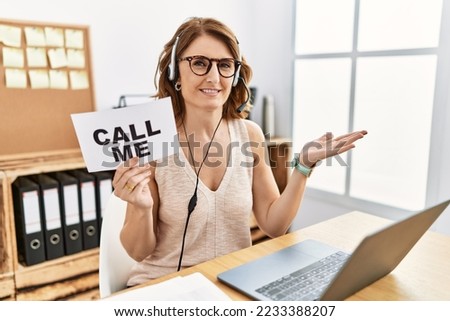 Middle age brunette woman wearing operator headset holding call me banner pointing aside with hands open palms showing copy space, presenting advertisement smiling excited happy 