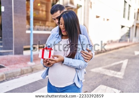 Young latin couple expecting baby surprise with gift at street