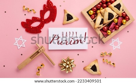 Purim celebration jewish carnival holiday concept. Tasty hamantaschen cookies, red carnival mask, noisemaker, sweet candies and party decor on pink background. Top view, flat lay, copy space.