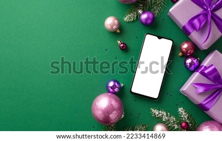 New Year celebration concept. Top view photo of smartphone lilac gift boxes with bows violet and pink baubles fir branches in snow and purple sequins on isolated green background with empty space