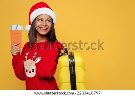 Traveler kid teen girl wear red sweater Santa hat hold bag passport ticket look aside isolated on plain yellow background Tourist travel abroad in free spare time rest getaway Air flight trip concept