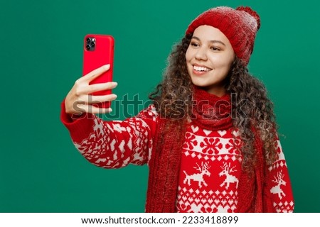Merry young woman wear red warm knitted sweater hat posing do selfie shot on mobile cell phone post photo on social network isolated on plain dark green background. Happy New Year 2023 holiday concept