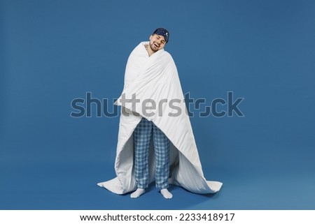 Full size body length young fun man 20s wear pajamas jam sleep mask resting relax at home wrap cover with blanket duvet look camera isolated on dark blue background Good mood night bedtime concept. Royalty-Free Stock Photo #2233418917