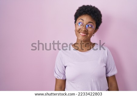 Young african american woman standing over pink background smiling looking to the side and staring away thinking. 