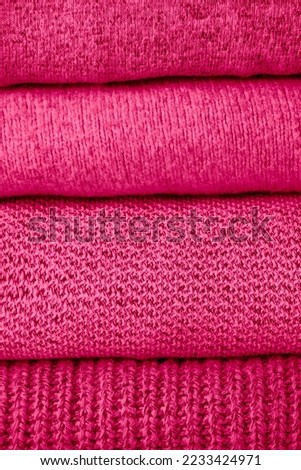 stack of warm magenta knit sweaters on white table and gray background. Cold autumn season texture detail