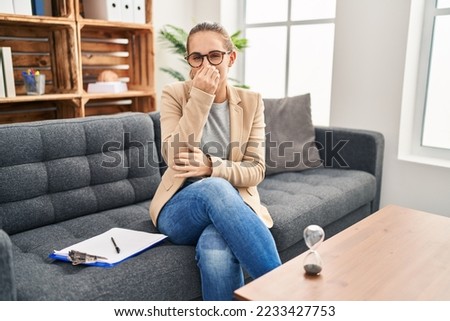 Young woman working at consultation office smelling something stinky and disgusting, intolerable smell, holding breath with fingers on nose. bad smell  Royalty-Free Stock Photo #2233427753