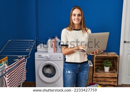 Young blonde woman smiling confident using laptop at laundry room