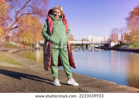 Mature woman on a walk in the autumn park in a green hoodie and long jacket, women's fashion. Royalty-Free Stock Photo #2233439933