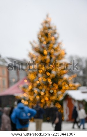 Blurred Christmas tree lights with bokeh. Outdoor advent gathering with silhouettes of blurred people