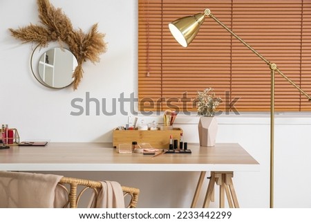 Box with makeup brushes, decorative cosmetics and flowers in vase on table near light wall Royalty-Free Stock Photo #2233442299