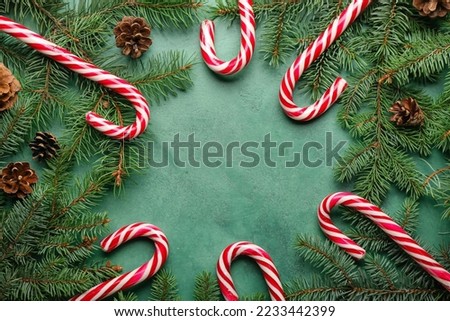 Frame made of sweet candy canes, fir branches and cones on color background