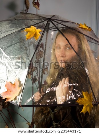 The main object of the image is a transparent umbrella,focusing on the umbrella,Woman under a transparent umbrella with autumn leaves,studio photo shoot