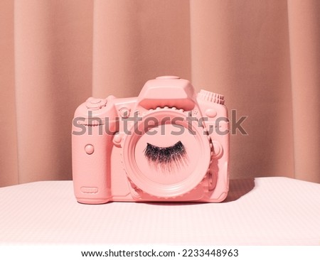 Photo camera model with false eyelashes on the lens, creative aesthetic pale pink layout. 