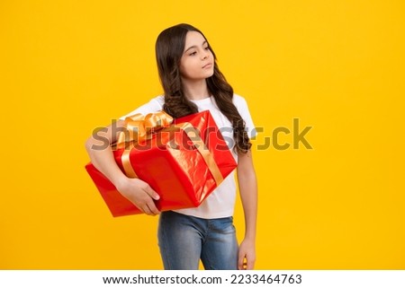 Portrait of a teenager child girl holding present box isolated over yellow studio background. Present, greeting and gifting concept. Birthday holiday concept.