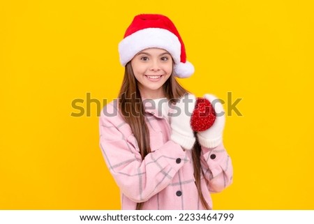 teen girl in mittens with red decorative ball on yellow background. xmas holiday decoration.
