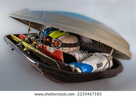 Car roof rack box with skis and equipment on a gray background.