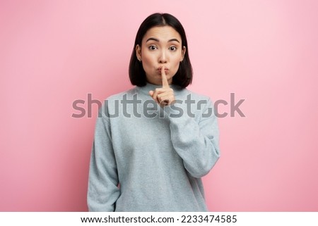 Shh, be quiet. Portrait of serious woman showing silence gesture with finger on her mouth, asking to stay quiet, keep secret. Indoor studio shot isolated on pink background 