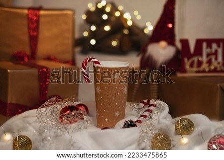 a cup of coffee or tea with a Christmas cozy design. Winter holiday decor, presents, fireplace with New Year golden light