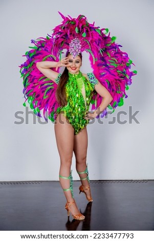 Young brunette girl dancer in a carnival costume of green and pink feathers poses on a white background